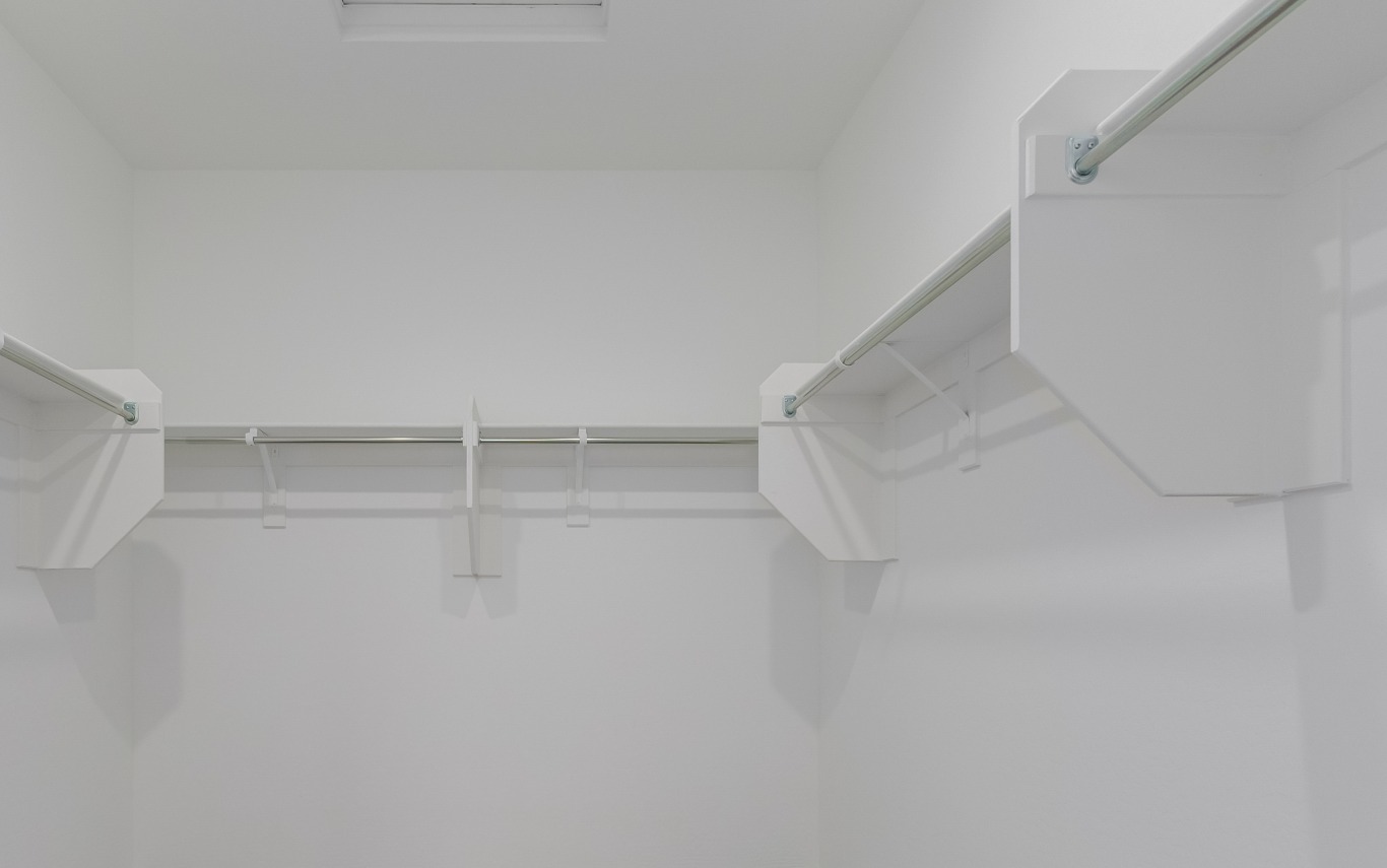 Empty white walk-in closet with multiple hanging rods and shelves attached to the walls.