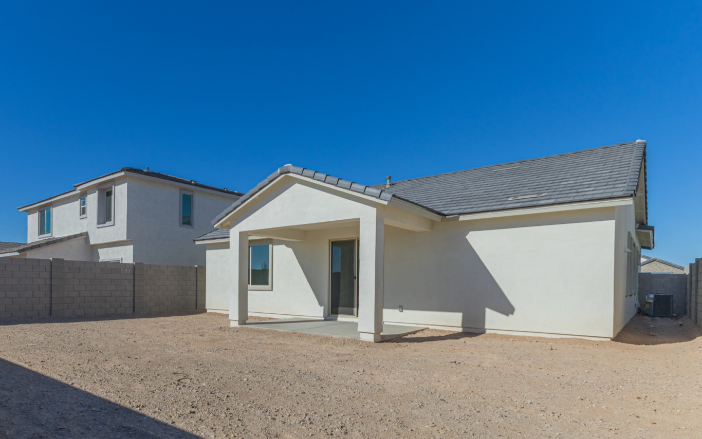 Single-story white house with gray roof, a covered patio, and no landscaping in the backyard; clear blue sky in the background.