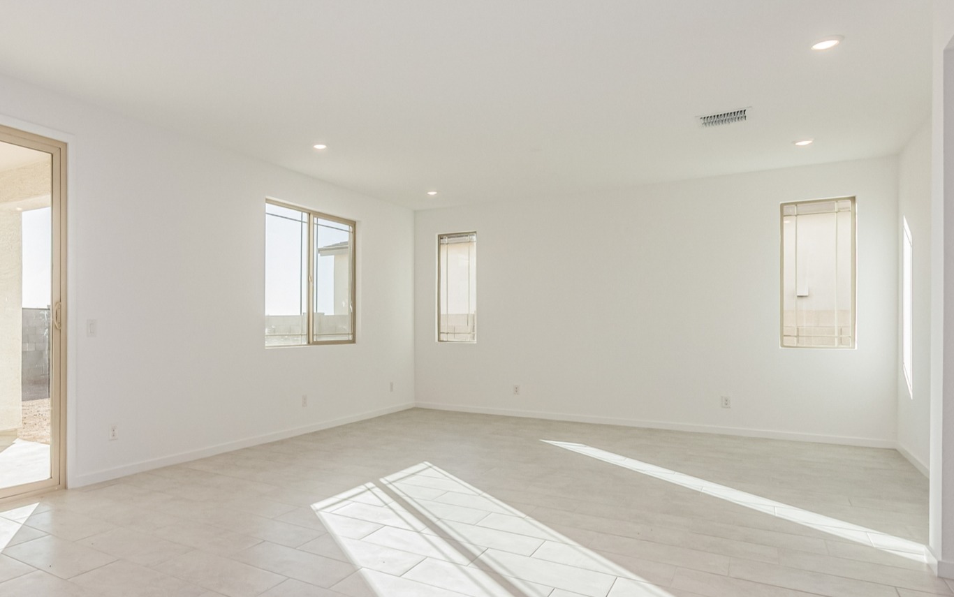 Empty, unfurnished room with white walls, large windows, recessed lighting, tiled floor, and sunlight streaming in through the windows.