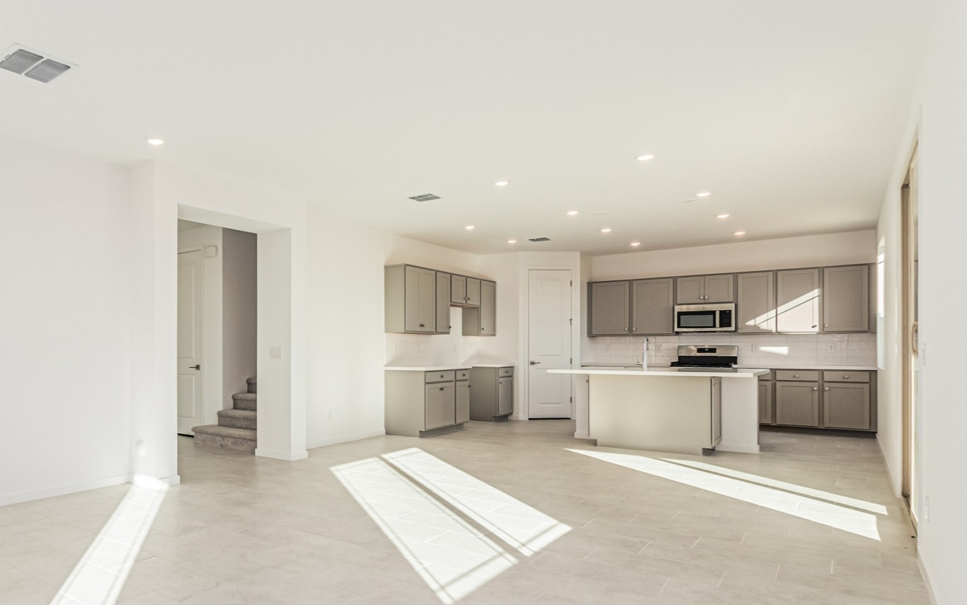 Spacious, modern kitchen with gray cabinets, stainless steel appliances, white walls, and large windows letting in natural light.