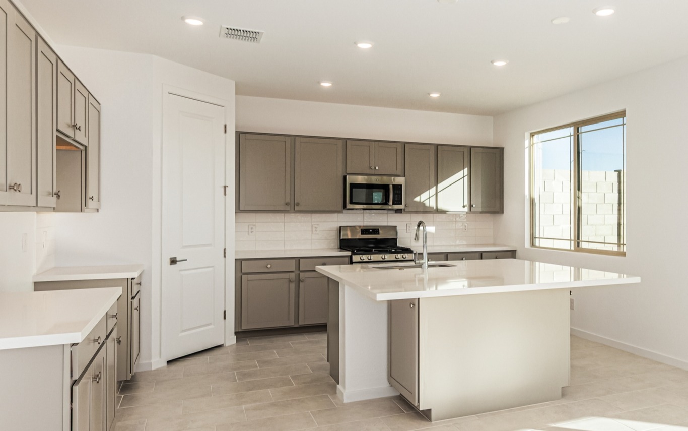 Modern kitchen with light gray cabinets, white countertops, stainless steel appliances, a center island, and a large window allowing natural light.