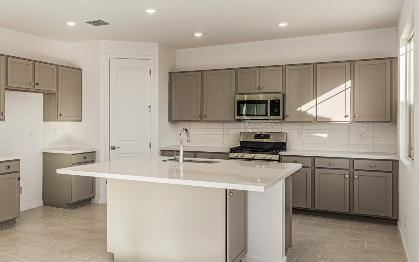 Modern kitchen with beige cabinets, white countertops, stainless steel appliances, a center island with sink, tiled floor, and recessed lighting.