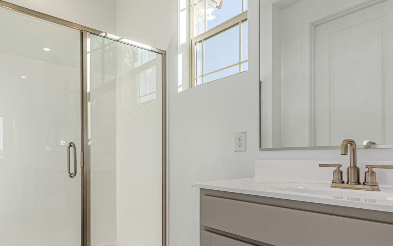 A modern bathroom with a glass shower enclosure, a white vanity with a sink, and a window letting in natural light.