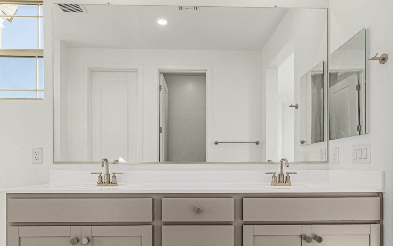 Modern bathroom vanity with double sinks, light grey cabinets, large mirror, towel bar on the right wall, and a window on the left. Walls and countertop are white.