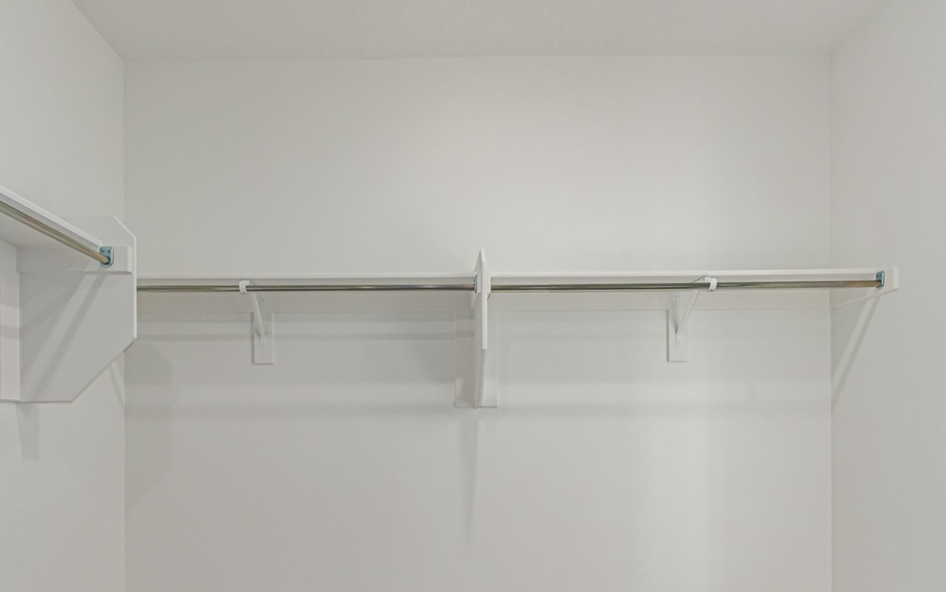 Empty white walk-in closet with metal hanging rods and wall-mounted shelves, viewed from inside.