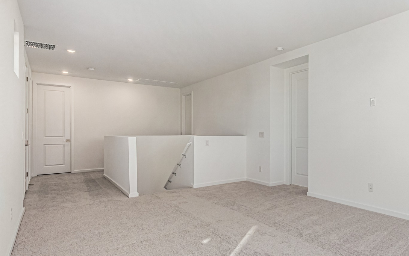 Unfurnished, carpeted upstairs hallway and open area with white walls, closed doors, and a stair railing on the right side.
