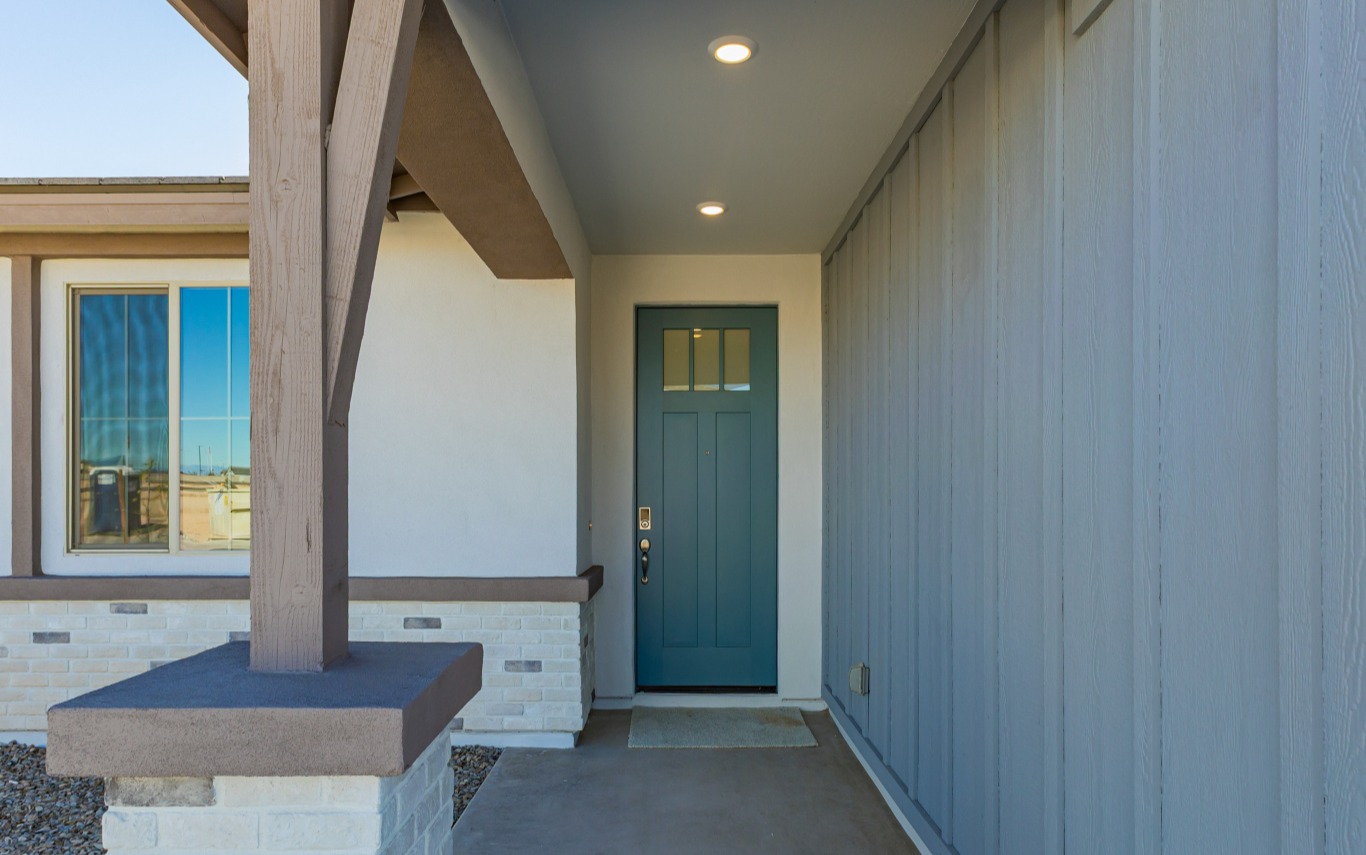 Covered front porch with a blue door, white brick and siding walls, a single window to the left, and overhead recessed lighting.