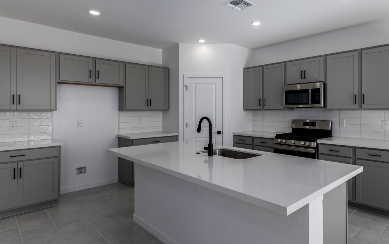 Modern kitchen with gray cabinets, white countertops, an island with a sink, stainless steel appliances, and tile flooring.
