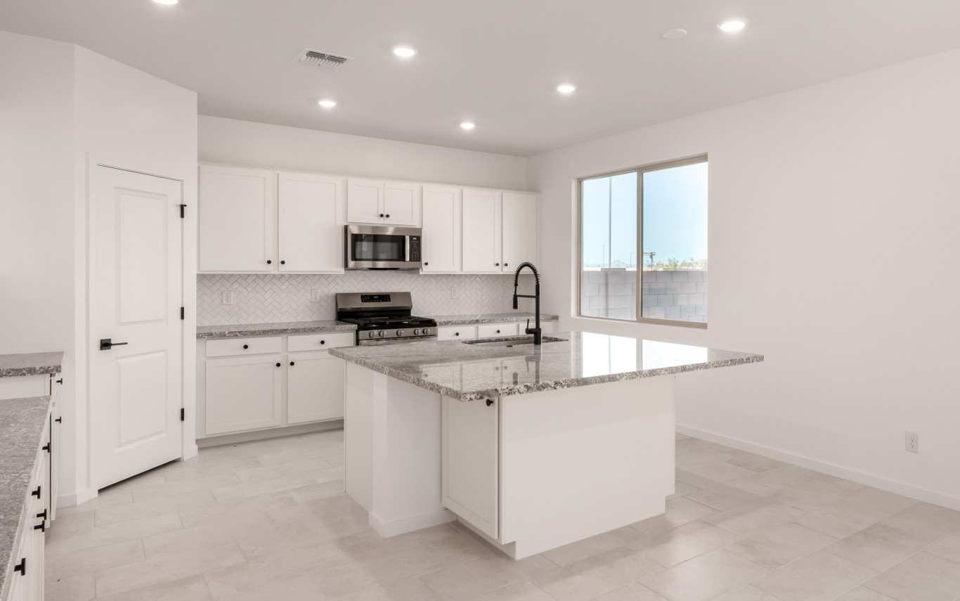 Modern kitchen with white cabinets, stainless steel appliances, granite countertops, a center island with a sink, tiled floor, and large window letting in natural light.