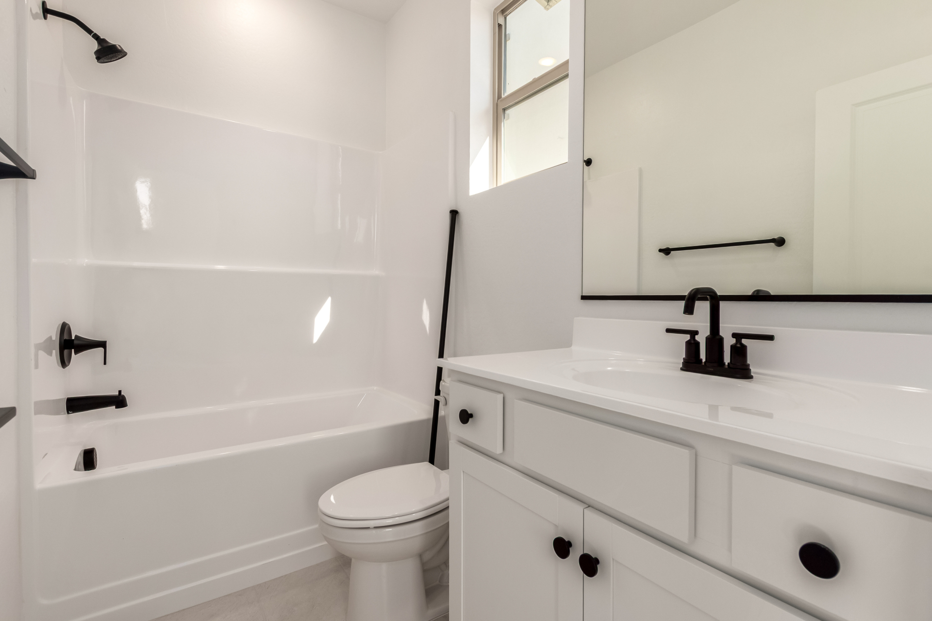 Modern white bathroom with a bathtub-shower combo, toilet, black fixtures, under-sink cabinet, and a large mirror above the sink.