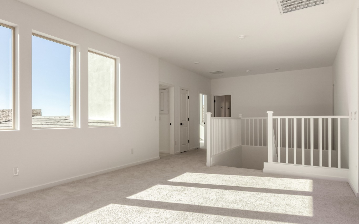 Bright, empty upstairs room with three windows, carpeted floor, white walls, a stair railing, and doors leading to other rooms.