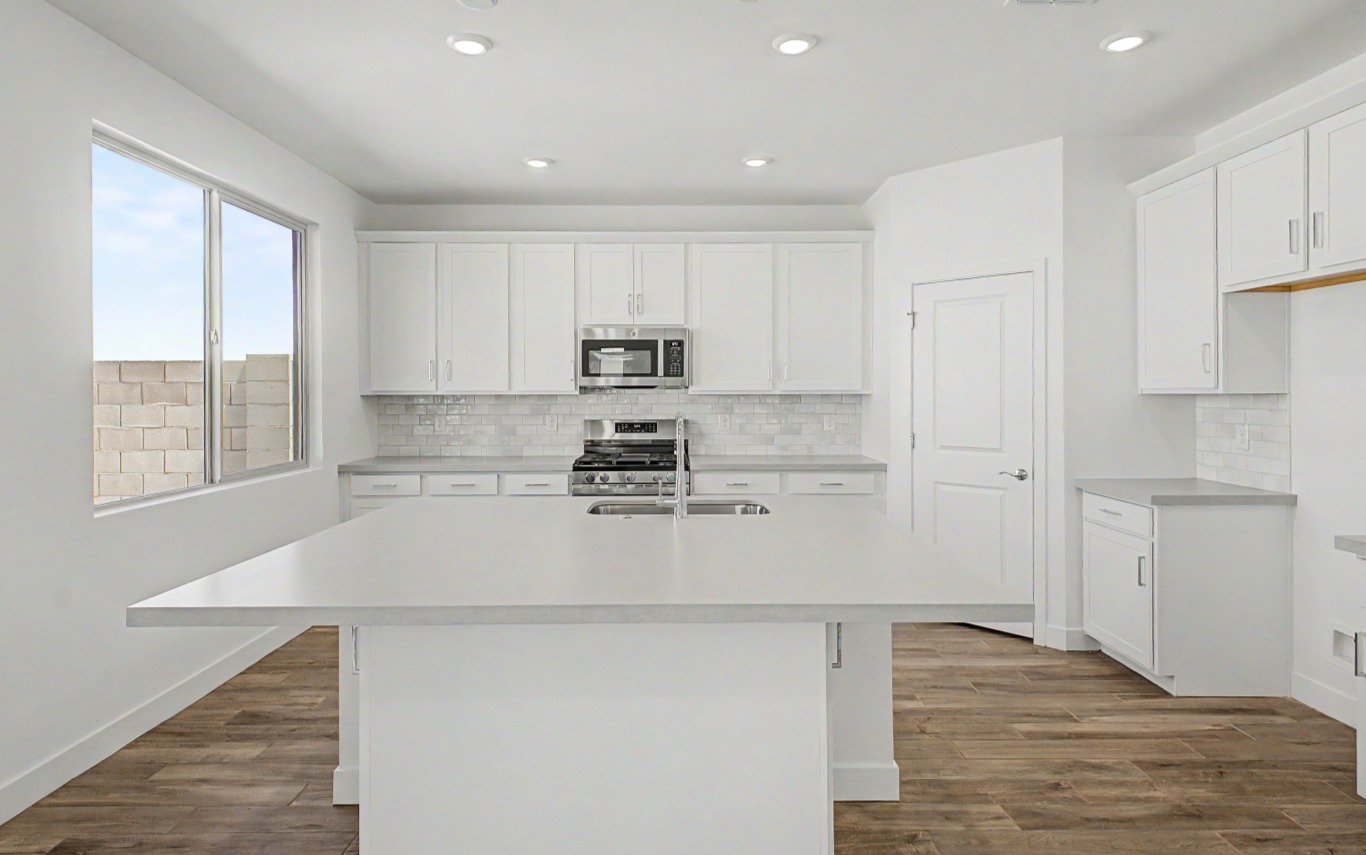 Modern kitchen with white cabinets, stainless steel appliances, subway tile backsplash, large window, and a central island on wood flooring.