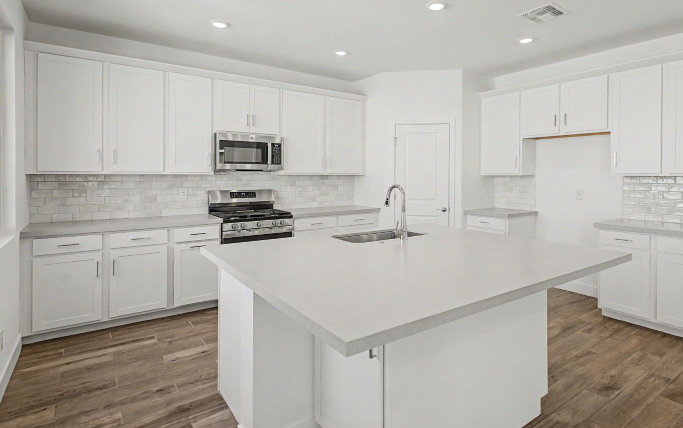 Modern kitchen with white cabinets, stainless steel appliances, subway tile backsplash, central island with sink, and wood-look flooring under bright overhead lighting.
