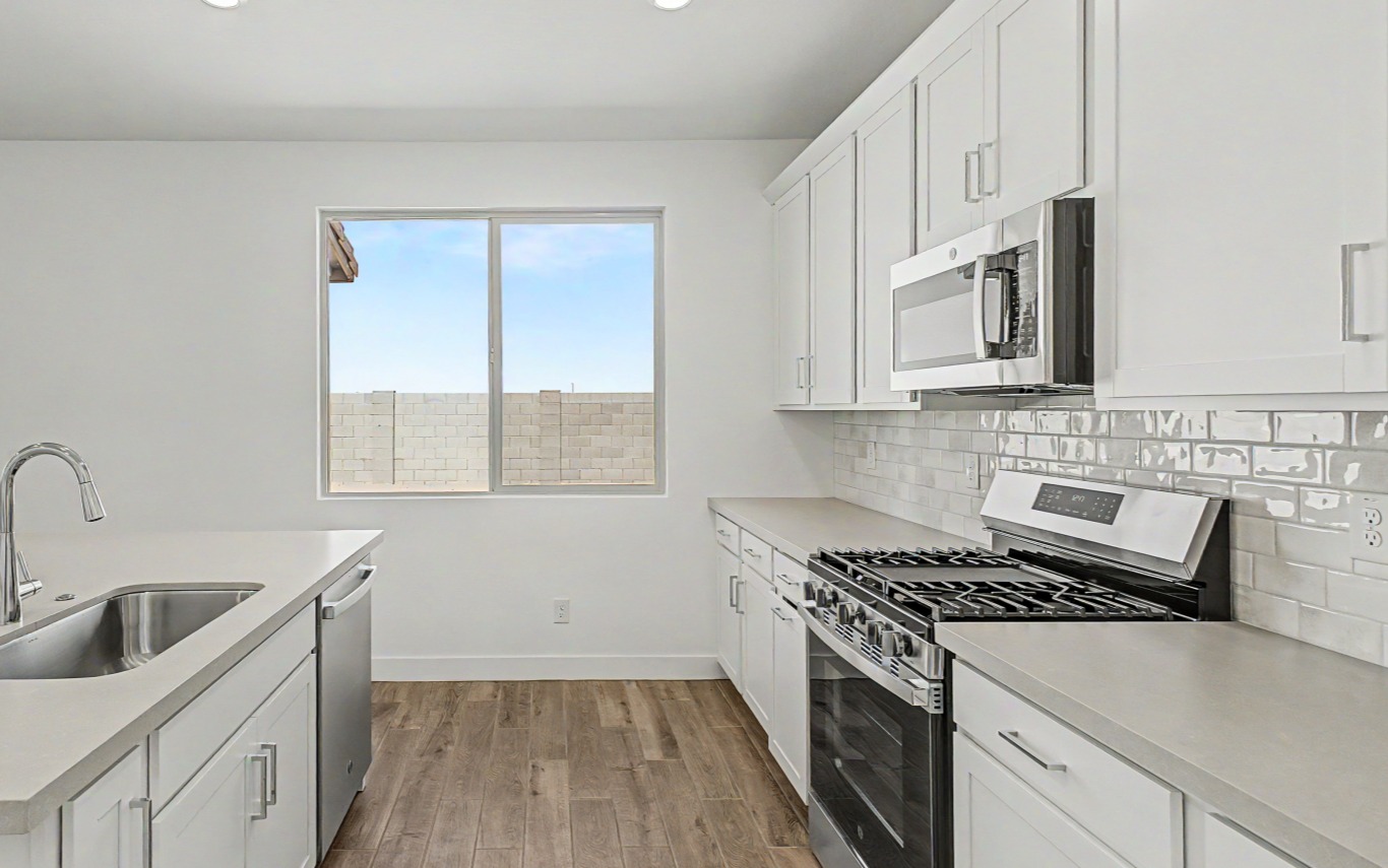Modern kitchen with white cabinets, stainless steel appliances, subway tile backsplash, and a window above wood-look flooring.