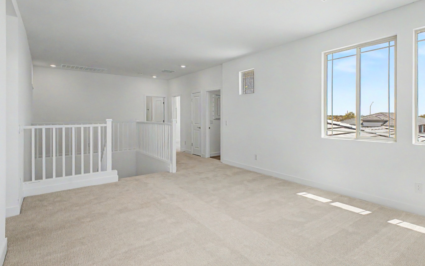 Bright upstairs hallway with beige carpet, white walls, stair railing, several doors, and large windows letting in natural light.