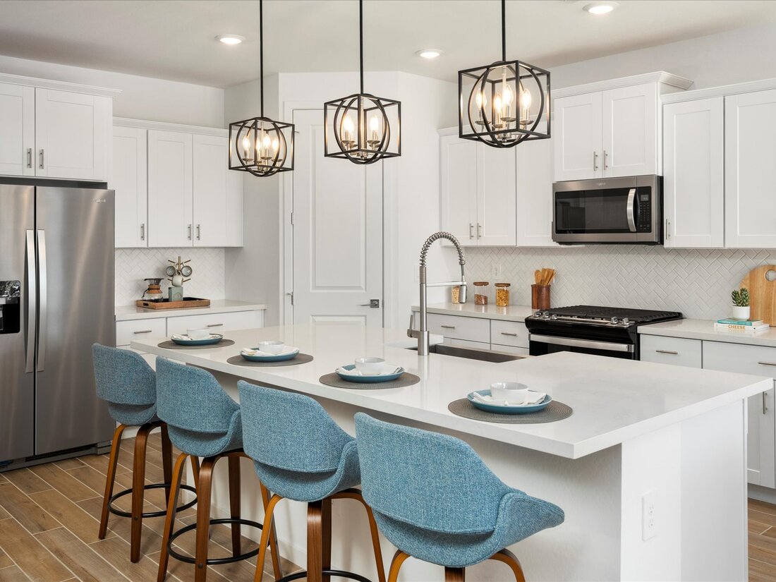 Modern kitchen with white cabinets, stainless steel appliances, a large island with blue barstools, pendant lights, and place settings on the counter.