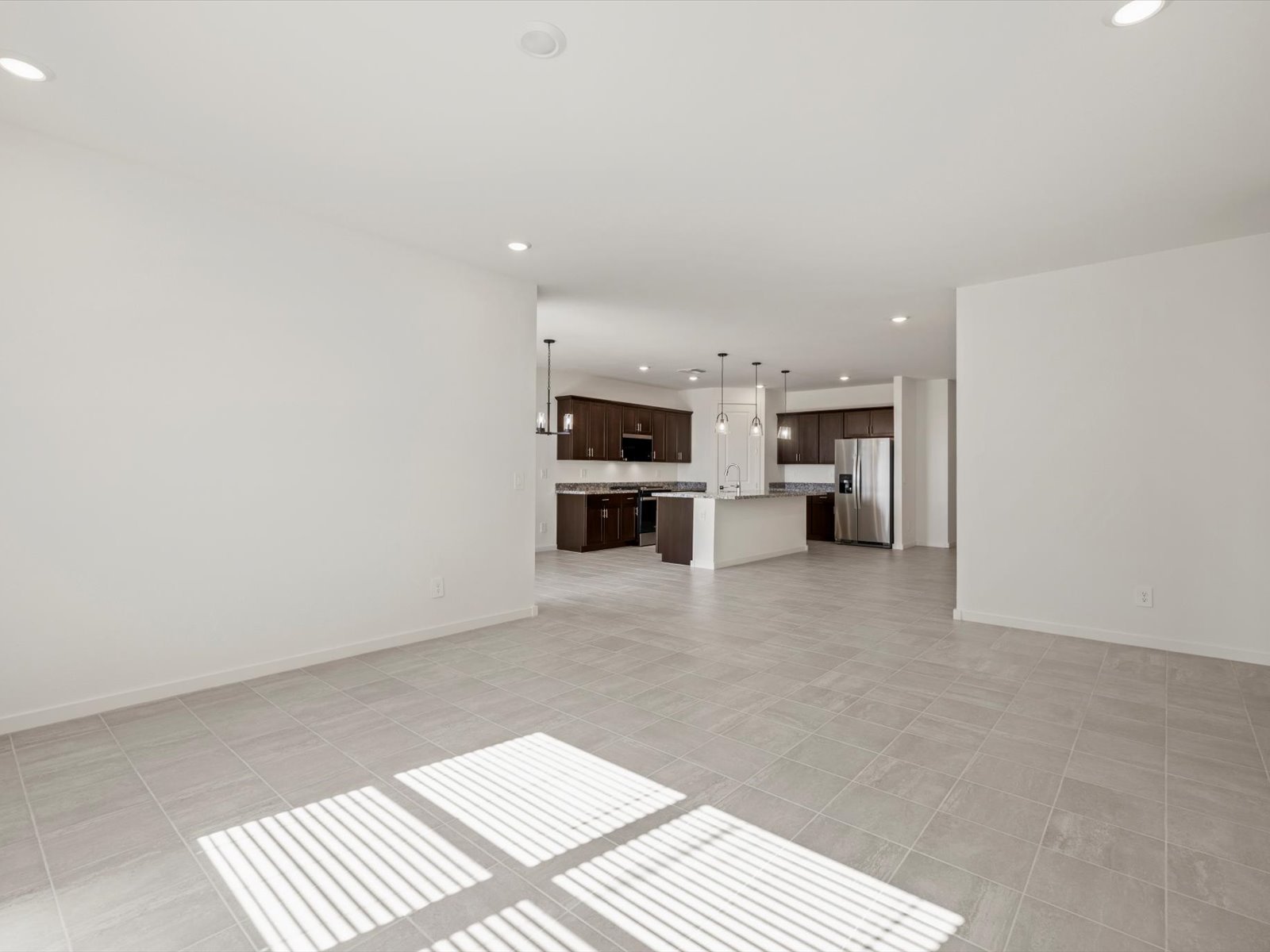 Spacious open-concept living area with tile floors, large windows, and a modern kitchen featuring dark cabinets, an island, and stainless steel appliances in the background.