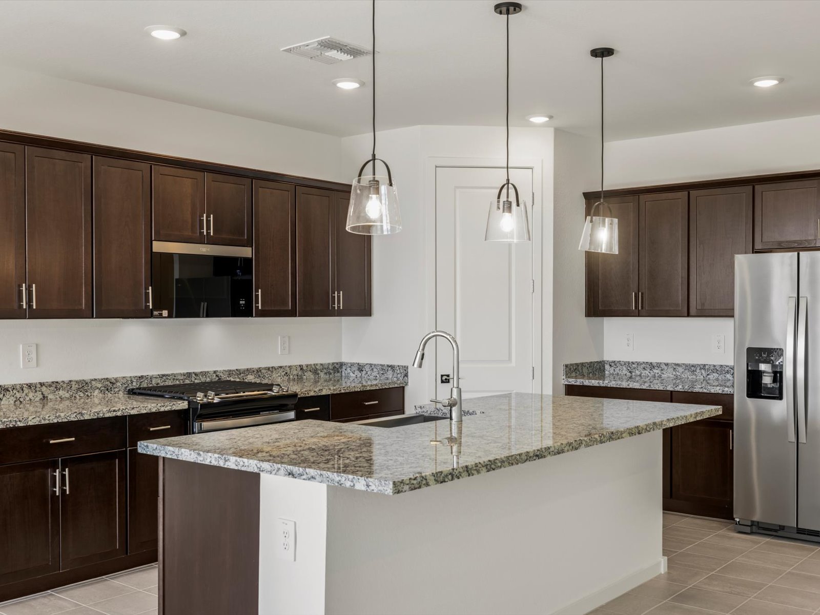 Modern kitchen with dark wood cabinets, granite countertops, stainless steel appliances, pendant lights, and a central island with a sink.