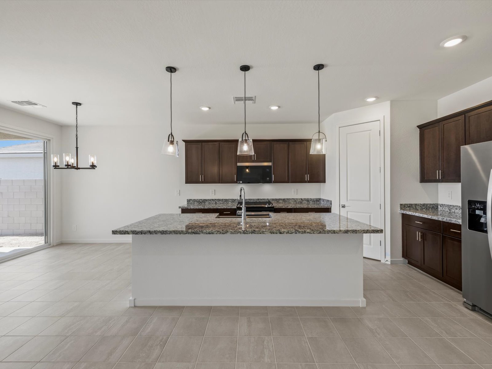 Modern kitchen with granite island, dark wood cabinets, stainless steel appliances, and pendant lighting, adjacent to a dining area with a chandelier and sliding glass door.