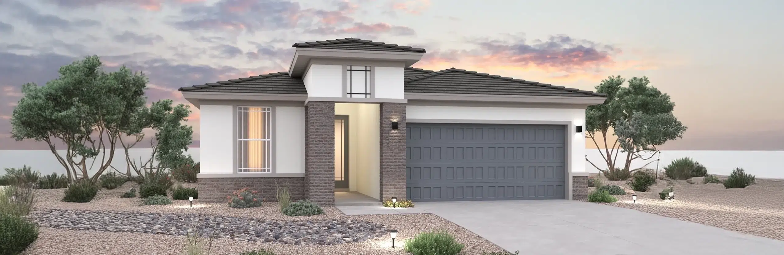 Modern single-story house with a two-car garage, flat tile roof, and desert landscaping, pictured at sunset with a cloudy sky in the background.