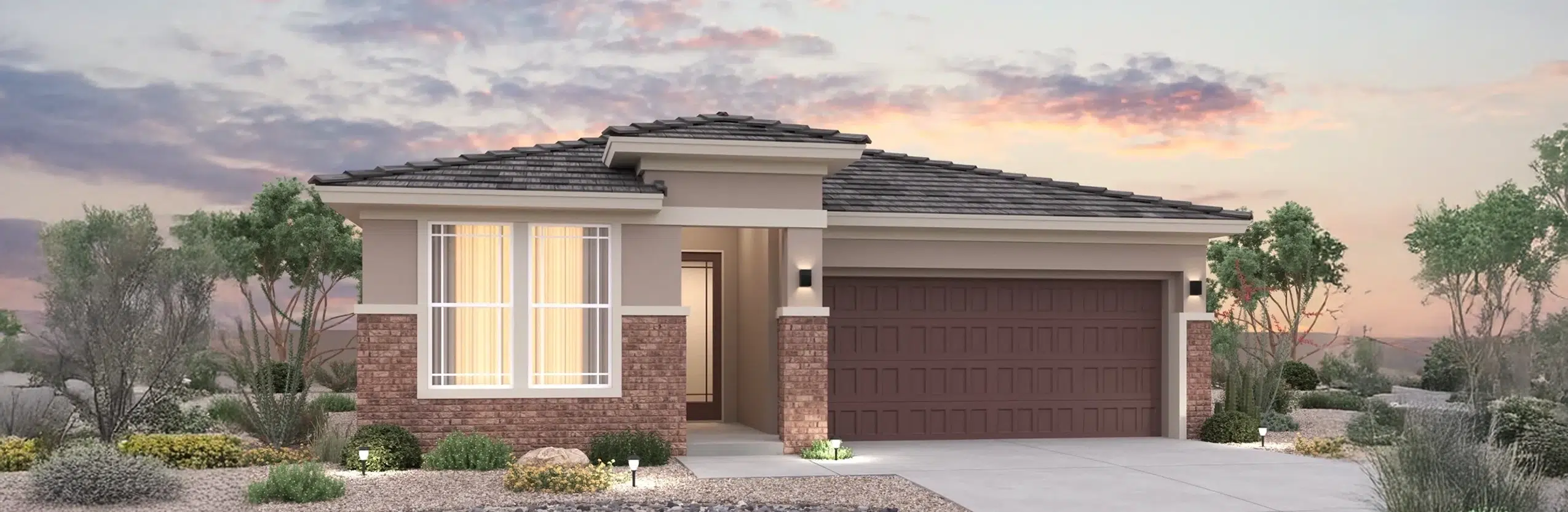 Single-story suburban house with brick and stucco exterior, large front windows, two-car garage, and desert landscaping at sunset.