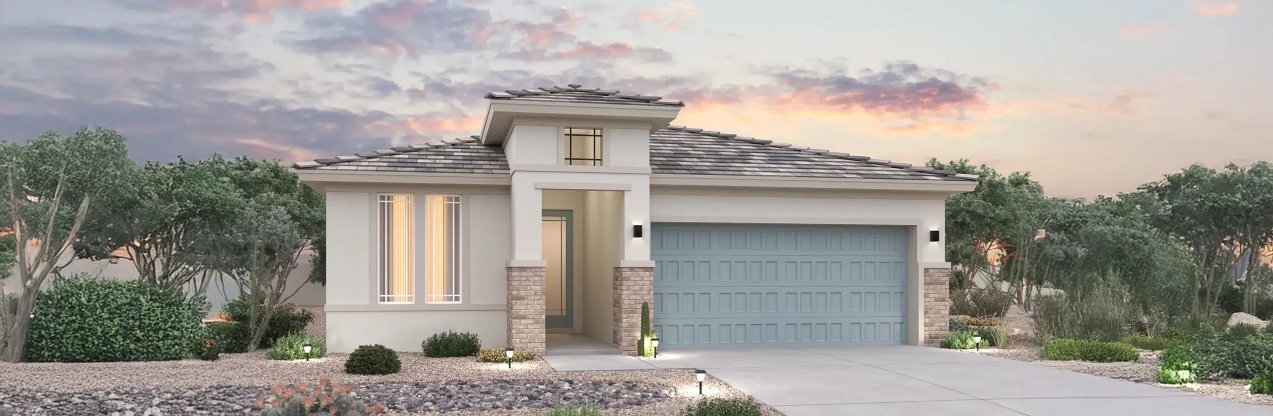 Modern single-story house with a gray tile roof, large windows, double garage, stone accents, and desert landscaping at sunset.