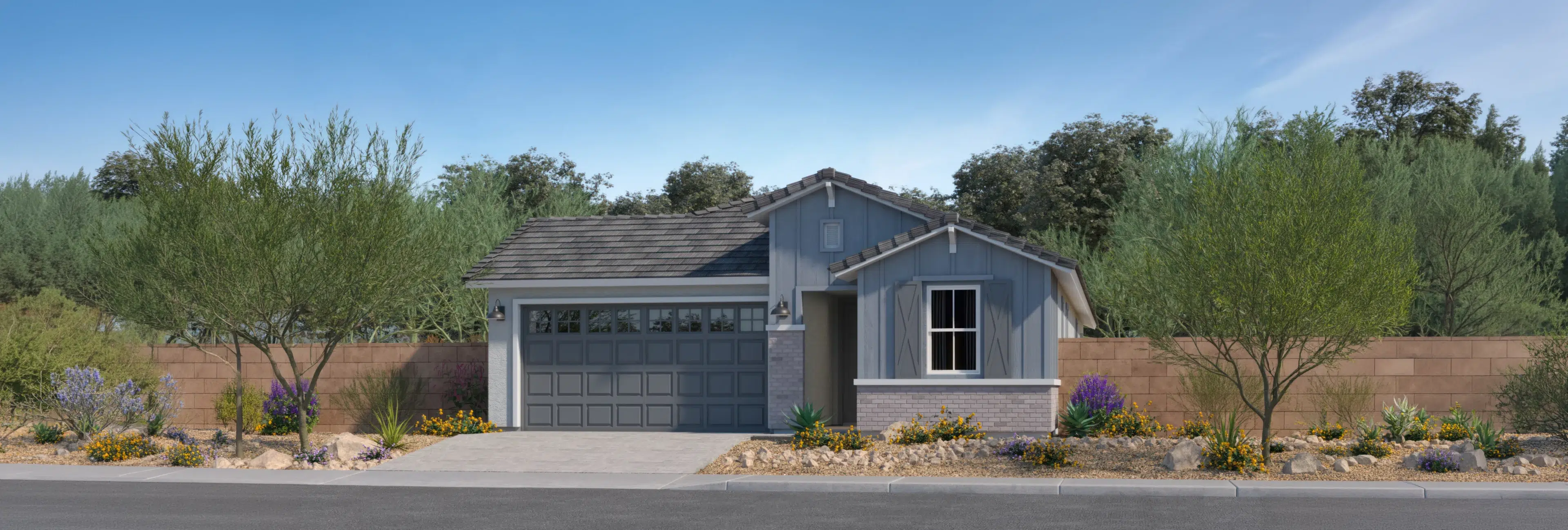Single-story house with gray siding and a two-car garage, surrounded by desert landscaping and bordered by a stone wall and trees in the background.