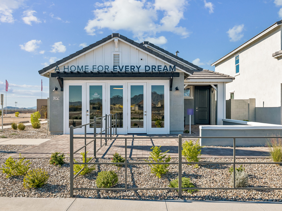 Single-story model home with a sign reading "A HOME FOR EVERY DREAM," large front windows, modern landscaping, and mountains visible in the background.
