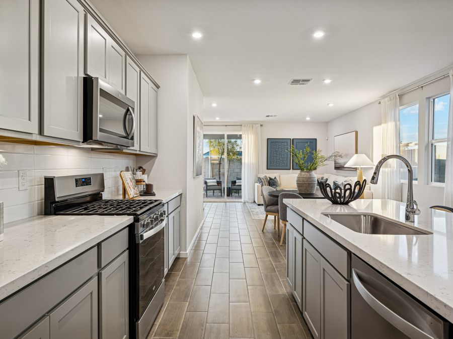 Modern kitchen with gray cabinets, stainless steel appliances, and a double sink, opening into a bright living area with large windows and a sliding glass door to the patio.
