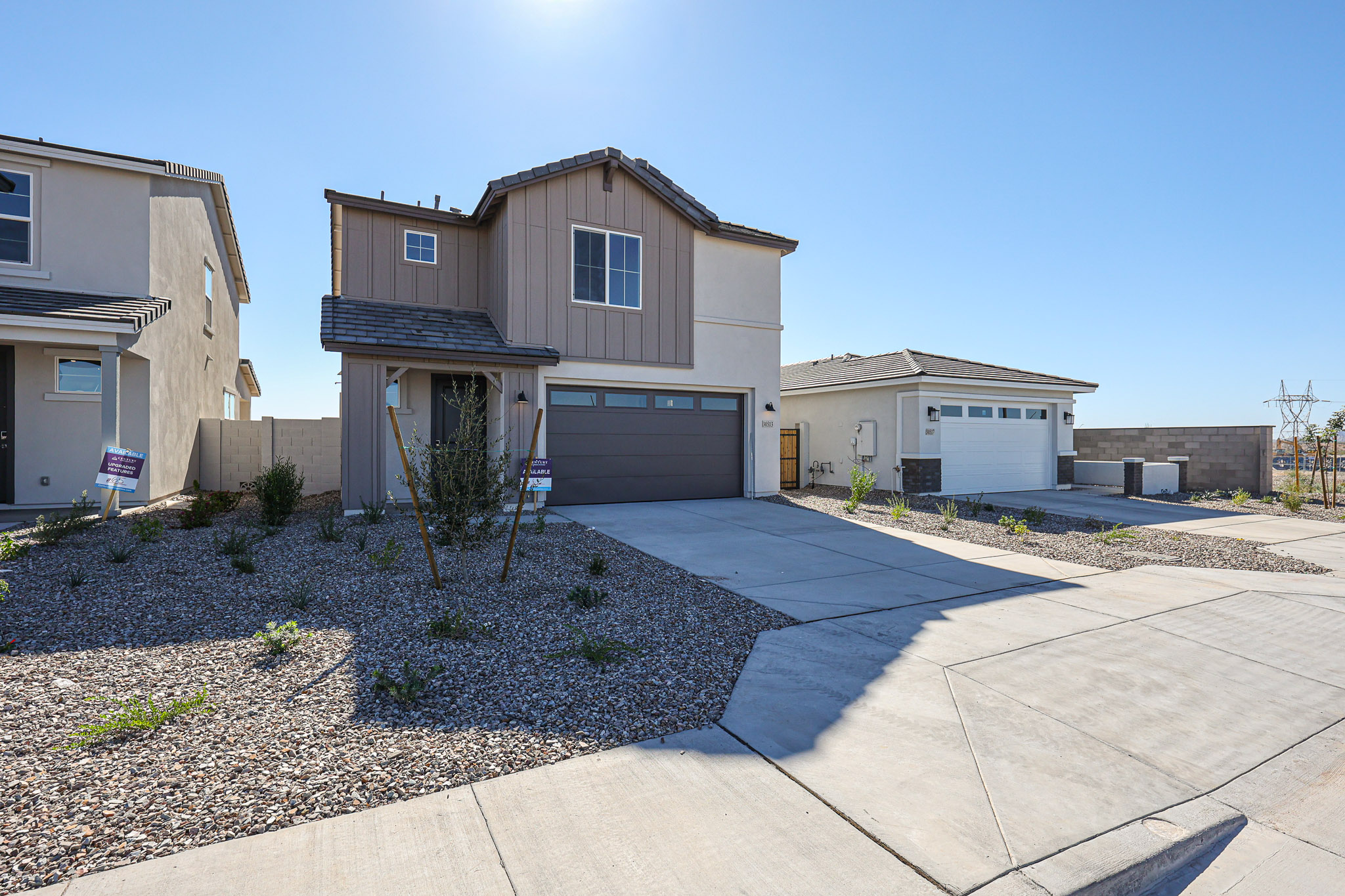 Two-story modern house with a double garage, tan siding, and a low-maintenance gravel front yard in a suburban neighborhood on a clear day.