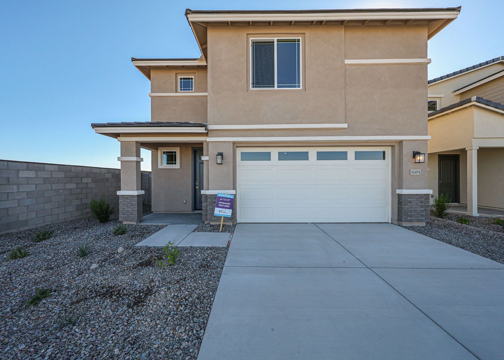 Two-story beige house with a double garage, gravel front yard, and a for sale sign near the entrance.