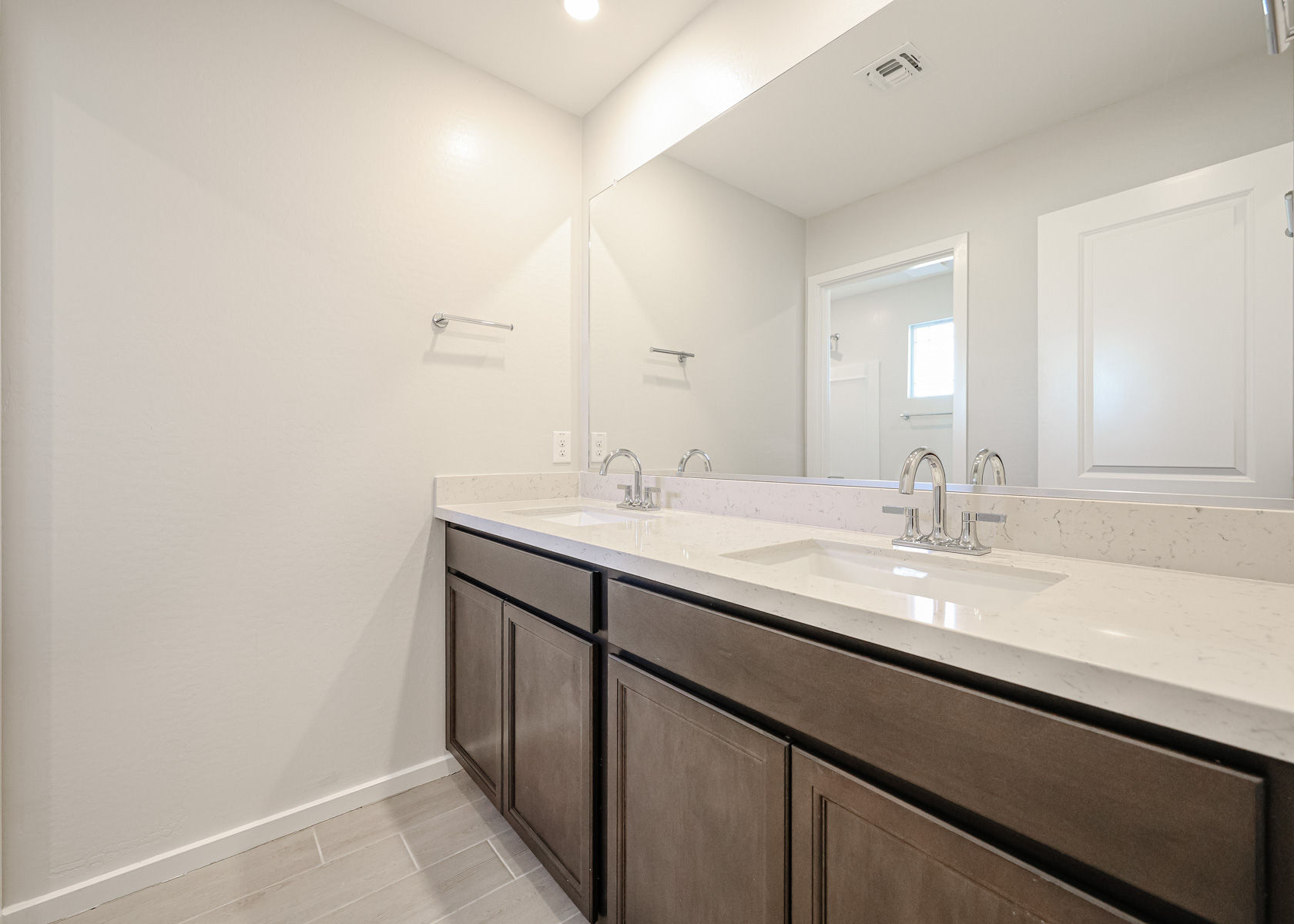 Modern bathroom with double sinks, marble countertop, dark wood cabinets, large mirror, and neutral-colored walls and floor.