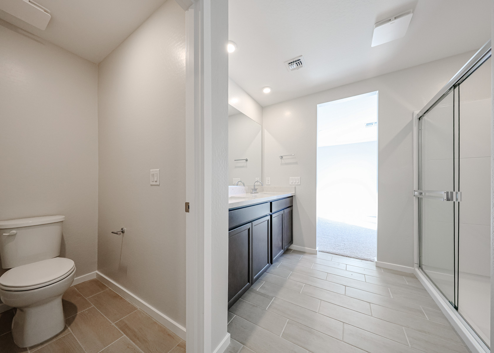 Modern bathroom with separate toilet area, double vanity with large mirror, neutral tile flooring, and a glass-enclosed shower.
