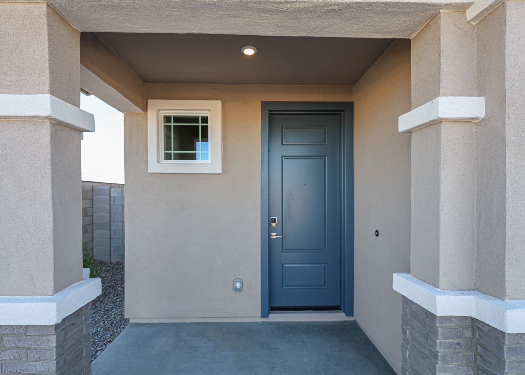 A modern entryway with a blue front door, a small window on the left, beige walls, and gray brick accents under a covered porch.
