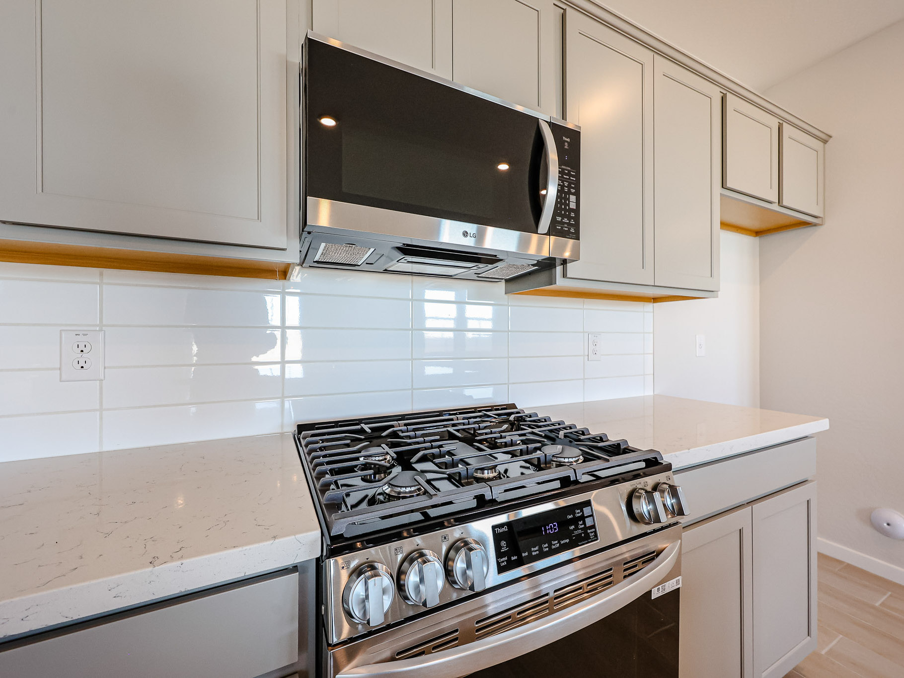 Modern kitchen with a stainless steel gas stove and oven, overhead microwave, gray cabinets, and white subway tile backsplash.