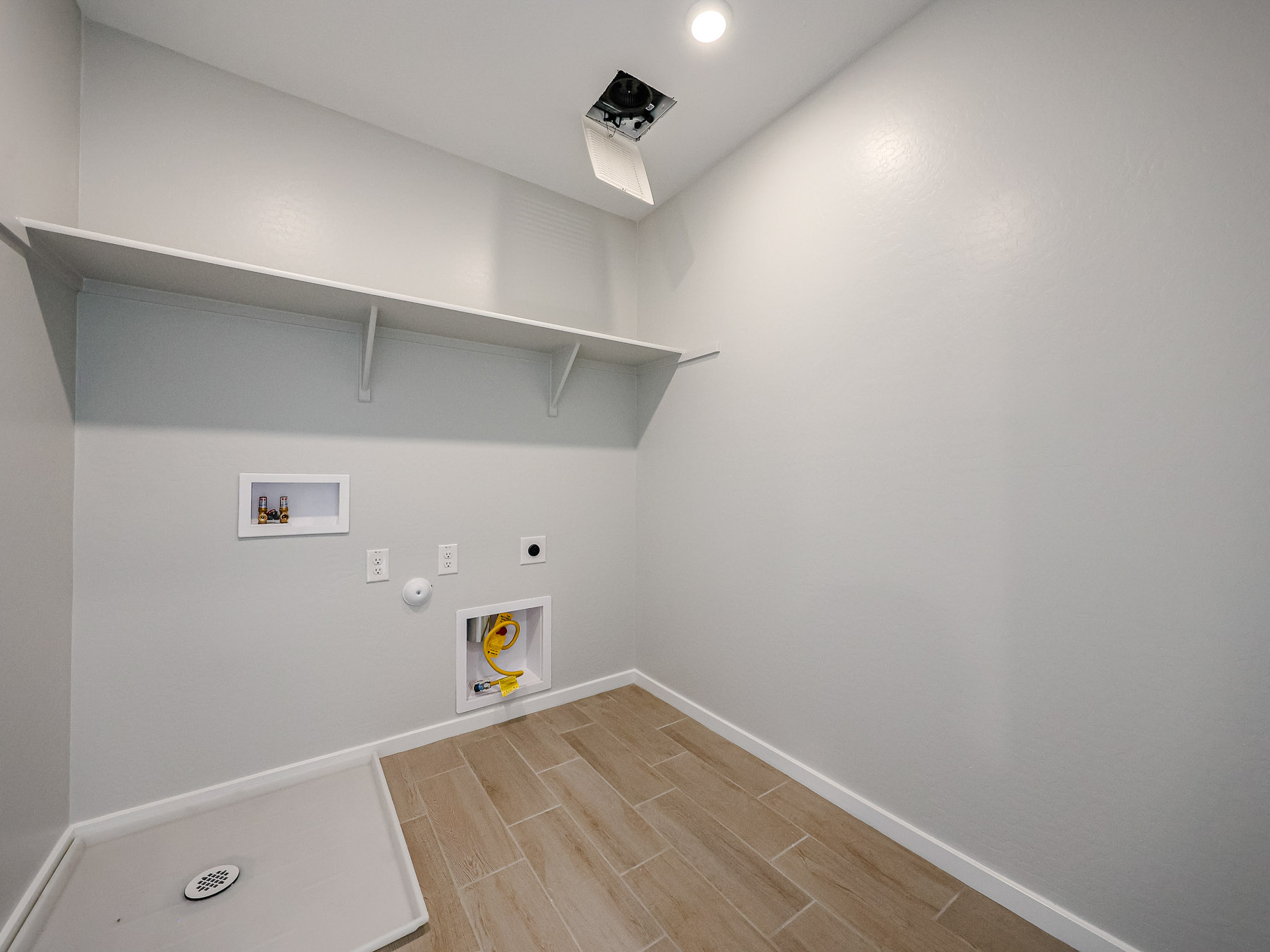 Empty laundry room with light gray walls, wood-look tile flooring, a built-in upper shelf, washer and dryer hookups, and a recessed ceiling light.