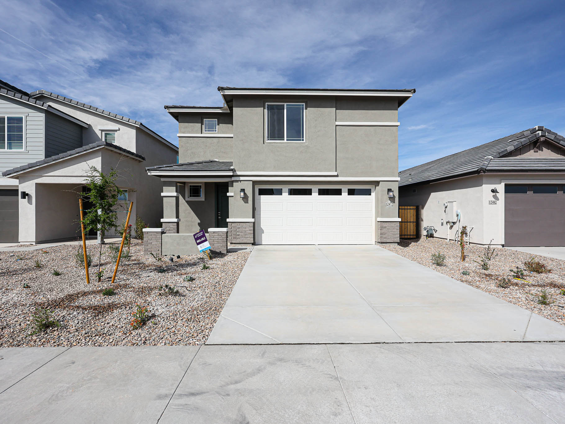 A modern two-story house with a double garage, gray exterior, and a rock-covered front yard with young trees and minimal landscaping.