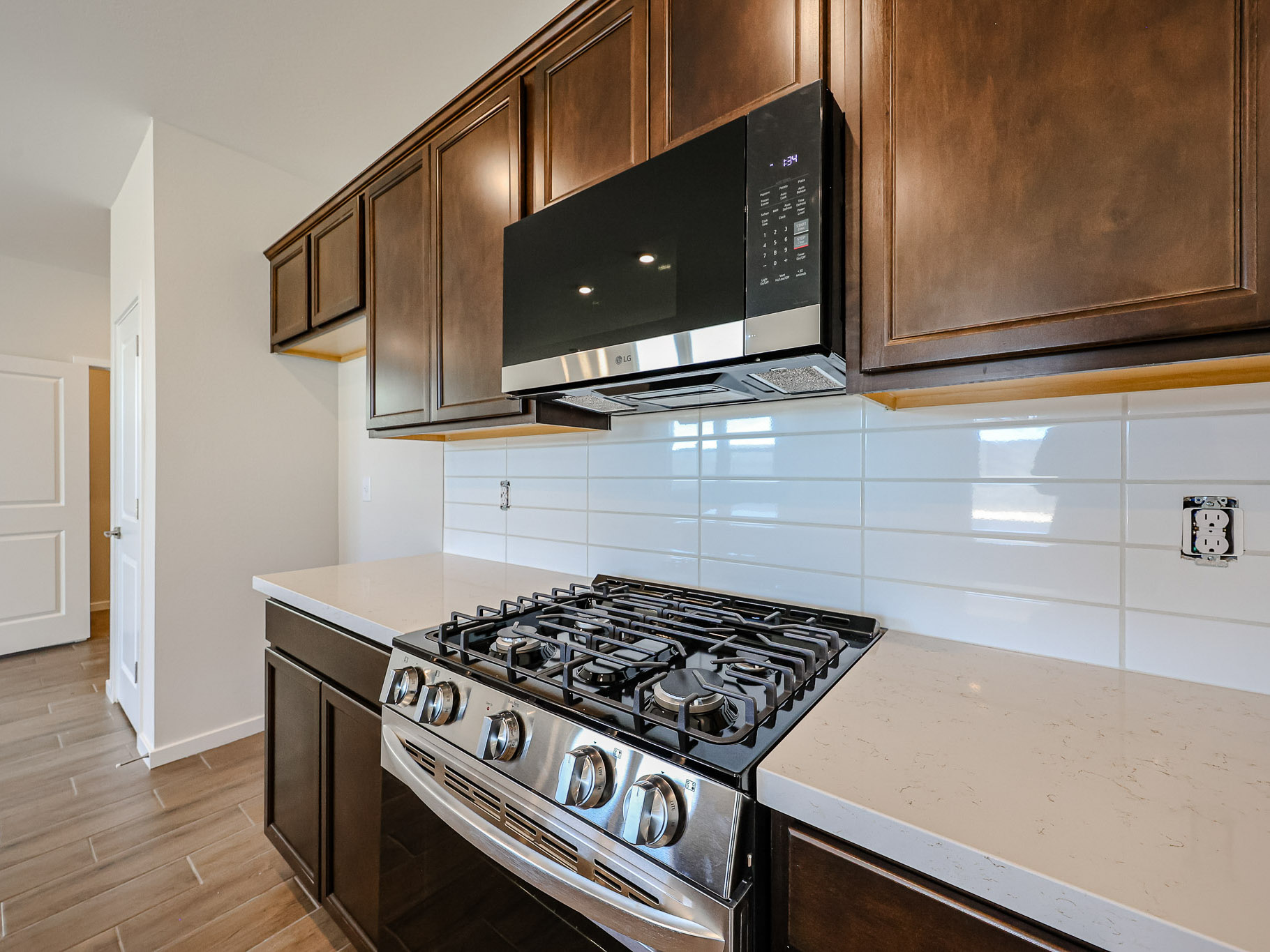 Modern kitchen with a stainless steel gas stove, overhead microwave, white tile backsplash, and dark wood cabinets.
