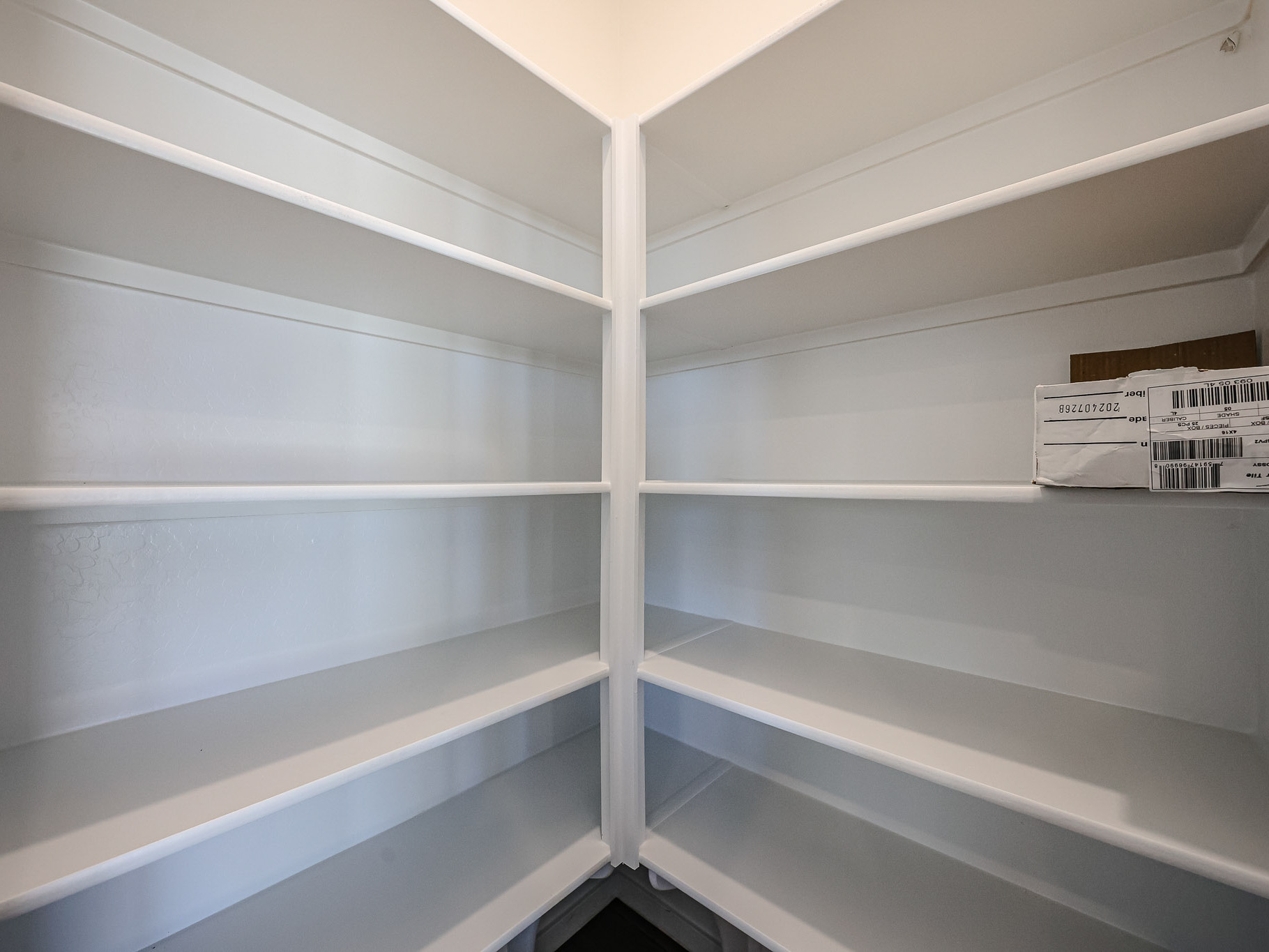 Empty white pantry shelves with a single cardboard box and a labeled package on the upper right shelf.