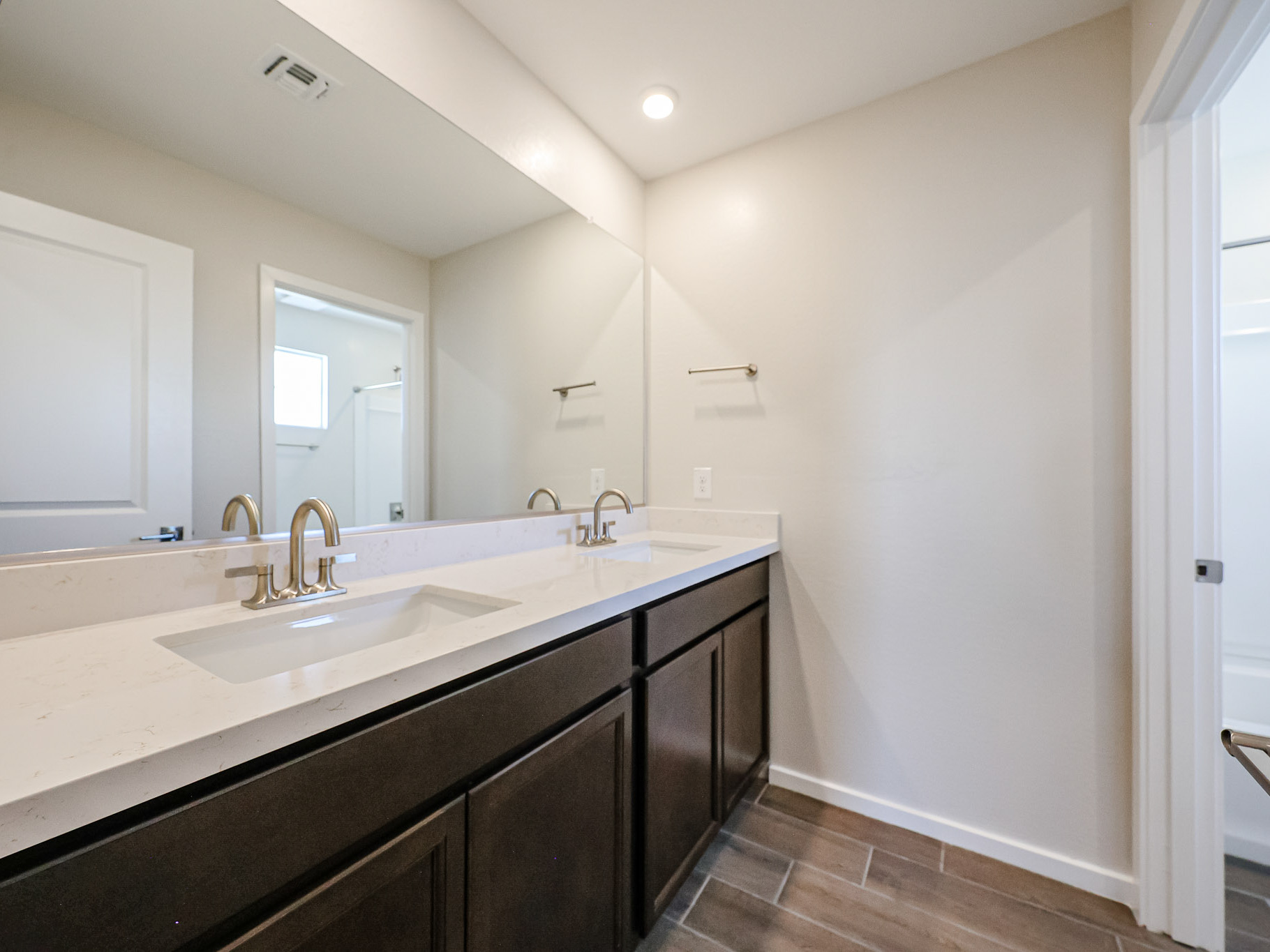 Modern bathroom with double sinks, dark wood cabinets, large mirror, and neutral-colored walls and floor; empty towel racks are visible on the wall.