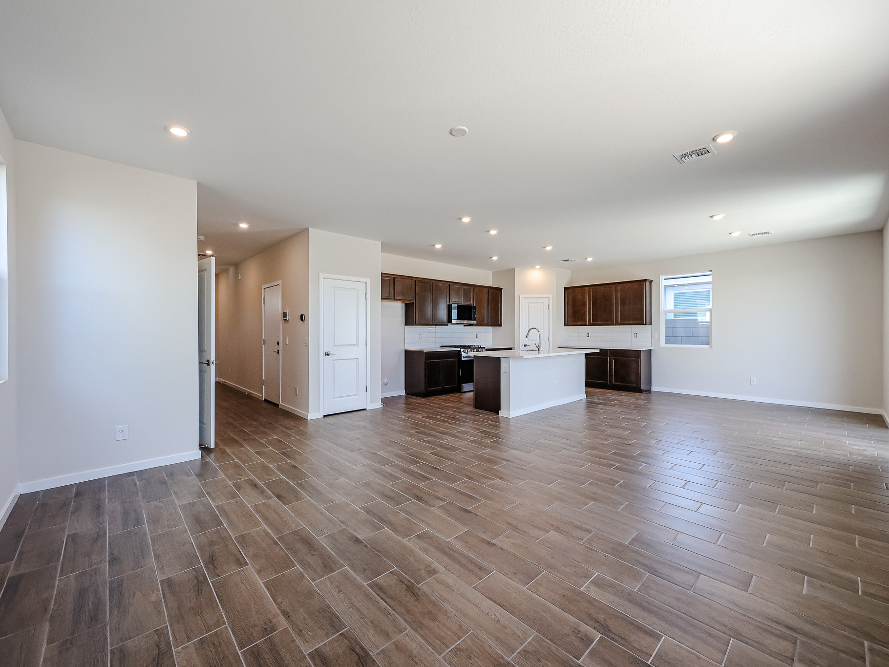 Spacious open-concept kitchen and living area with wood-look tile flooring, white walls, recessed lighting, and large windows.