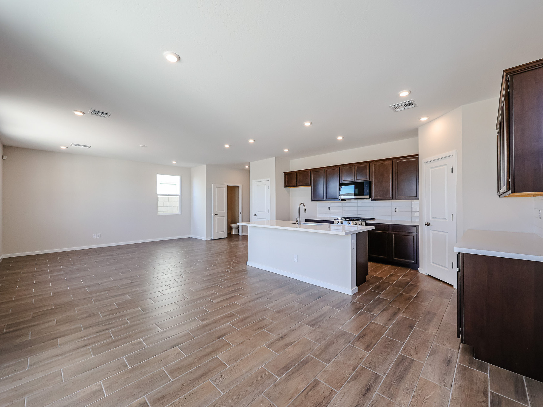 Spacious open-concept kitchen and living area with wood-look tile flooring, dark cabinets, white countertops, and recessed lighting.