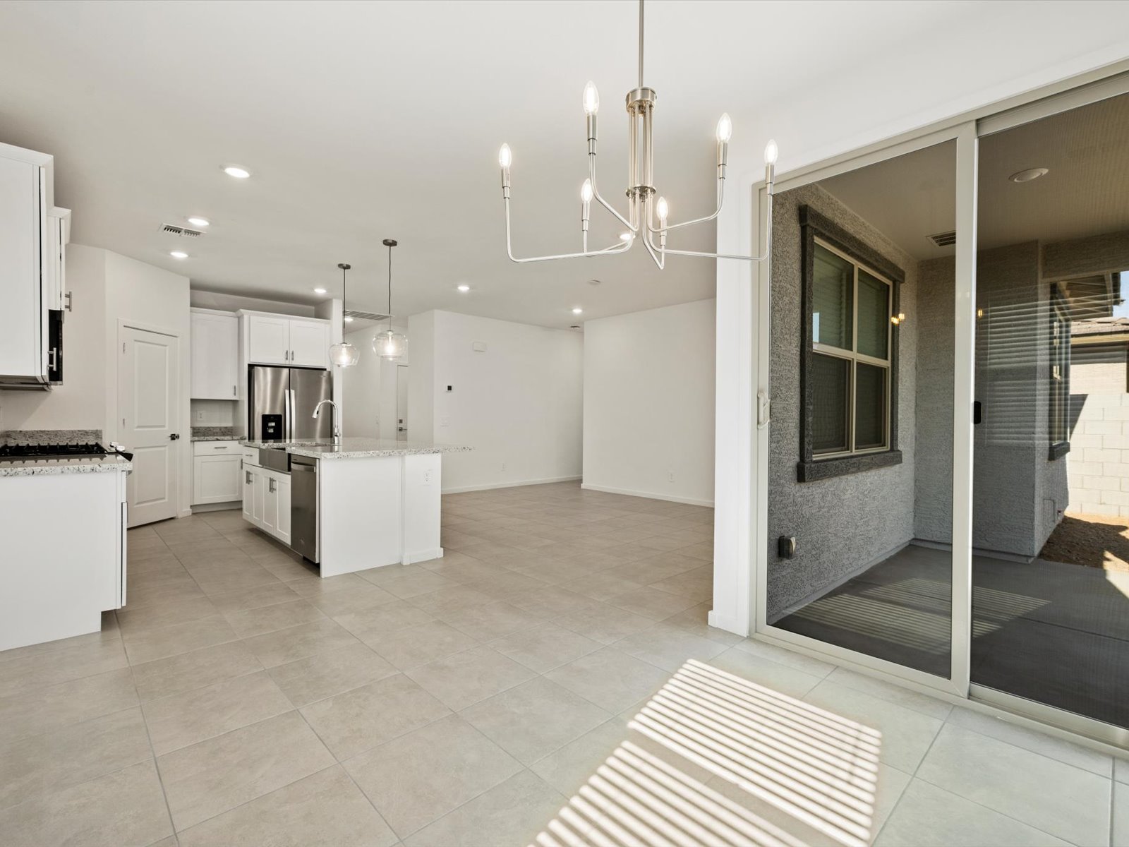 Modern open-concept kitchen and living area with white cabinets, stainless steel appliances, tile flooring, island, and sliding glass doors leading to a covered patio.