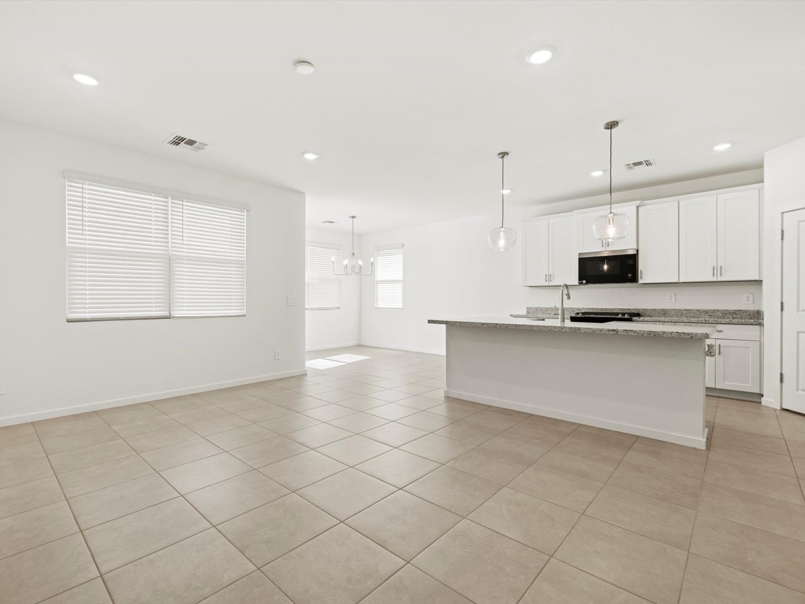 Spacious, modern open-plan kitchen and living area with tiled floors, white cabinets, granite countertops, and large windows allowing natural light.