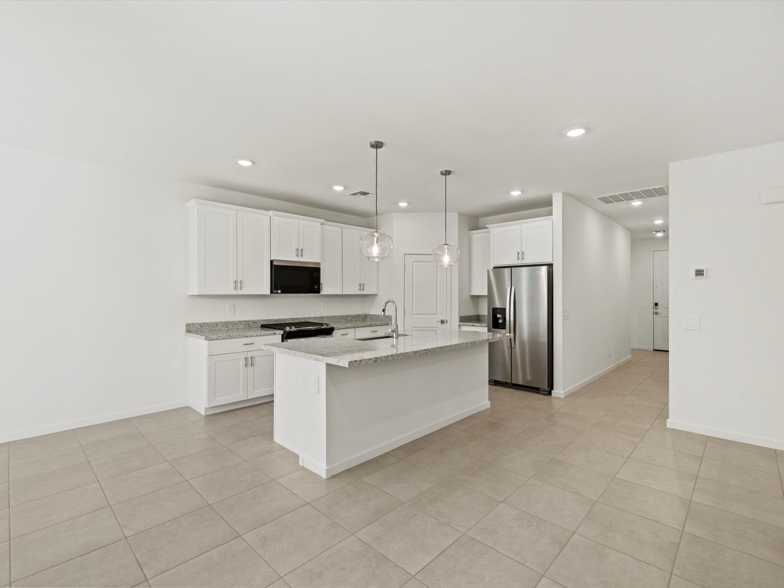 Modern kitchen with white cabinets, stainless steel appliances, granite countertops, center island with pendant lights, and beige tile flooring in a spacious open layout.
