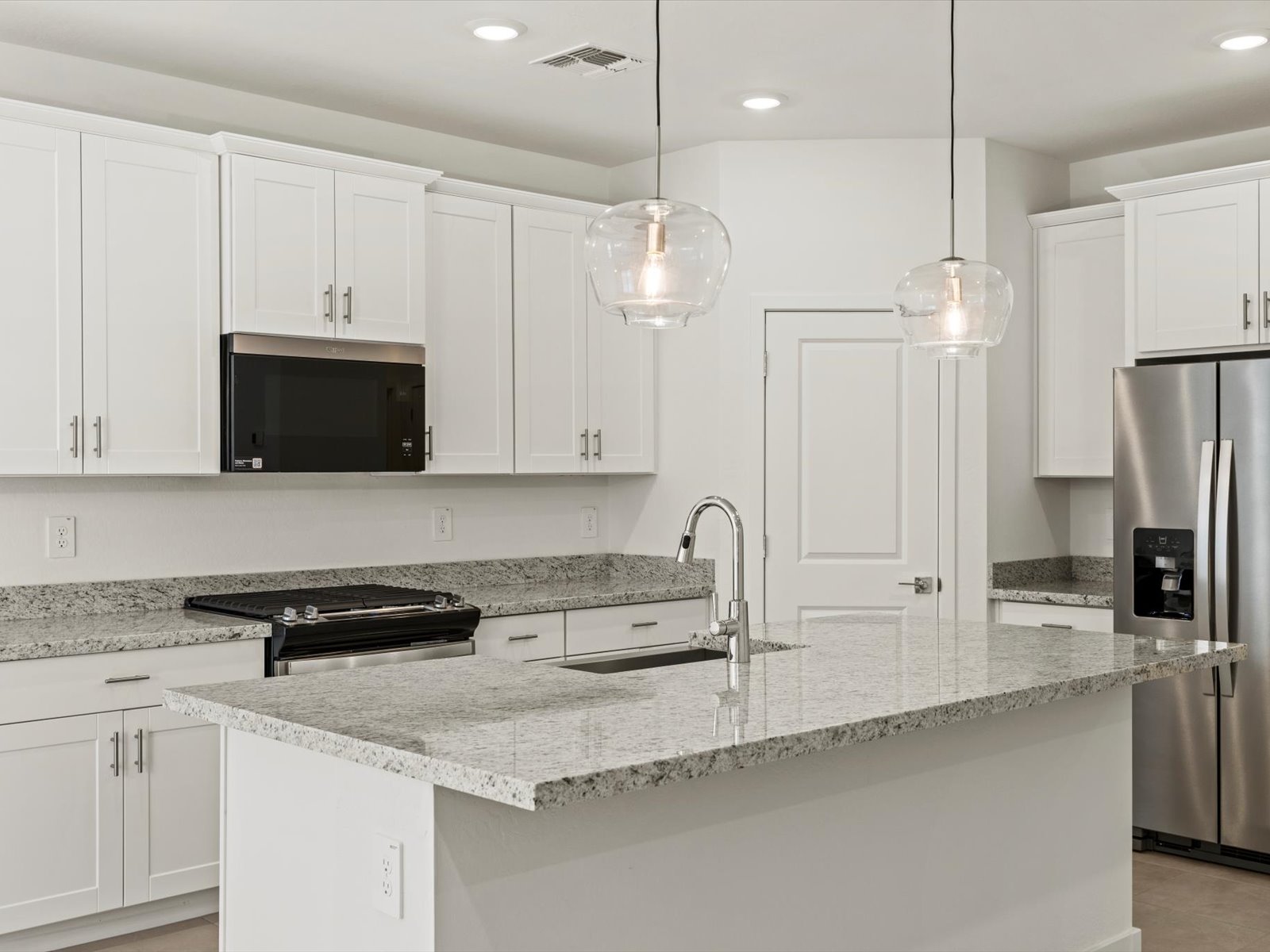 Modern kitchen with white cabinets, granite countertops, stainless steel appliances, pendant lights, and an island with a sink.