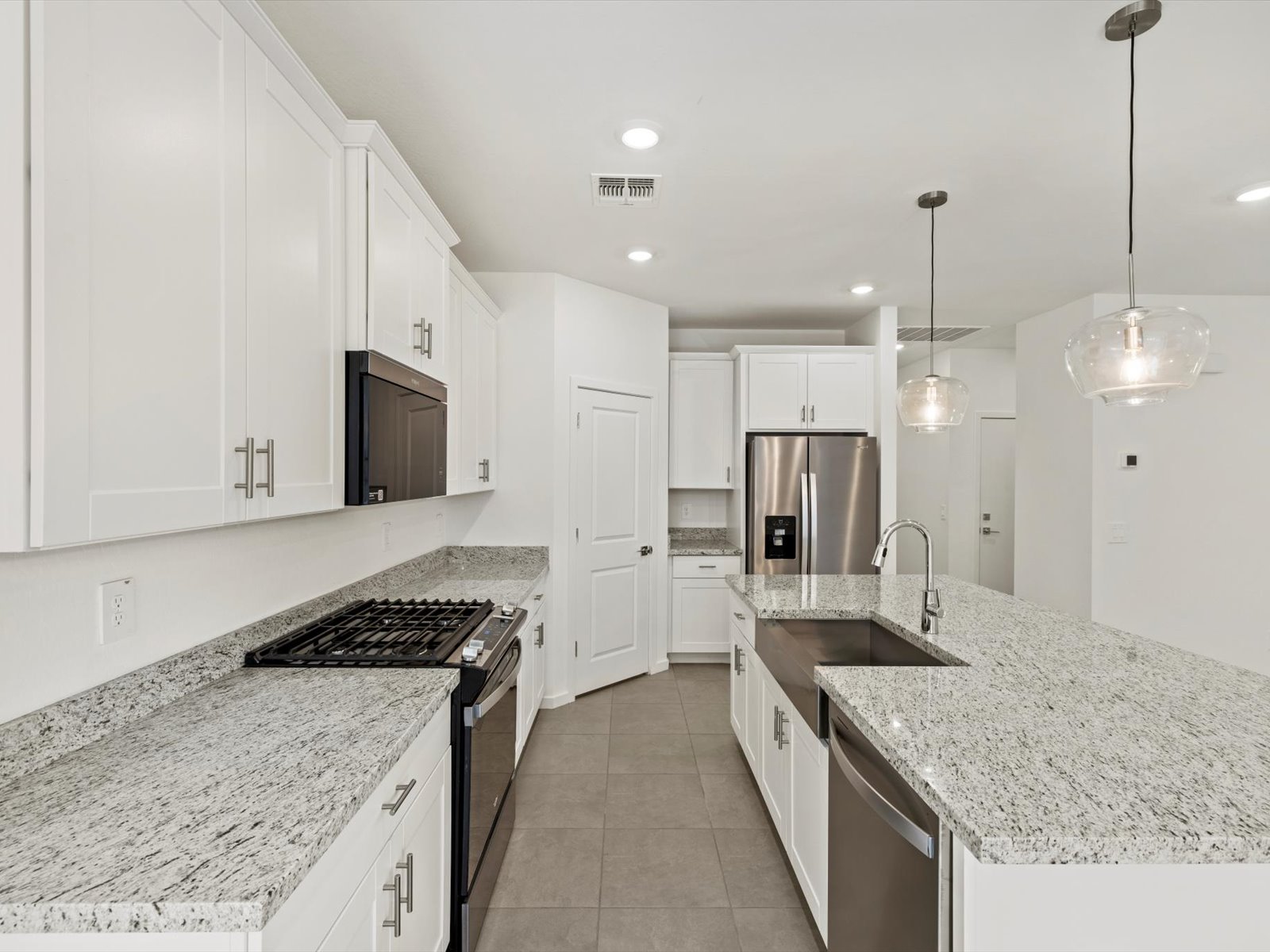 Modern kitchen with white cabinets, stainless steel appliances, granite countertops, double sink, and two pendant lights above a large island.