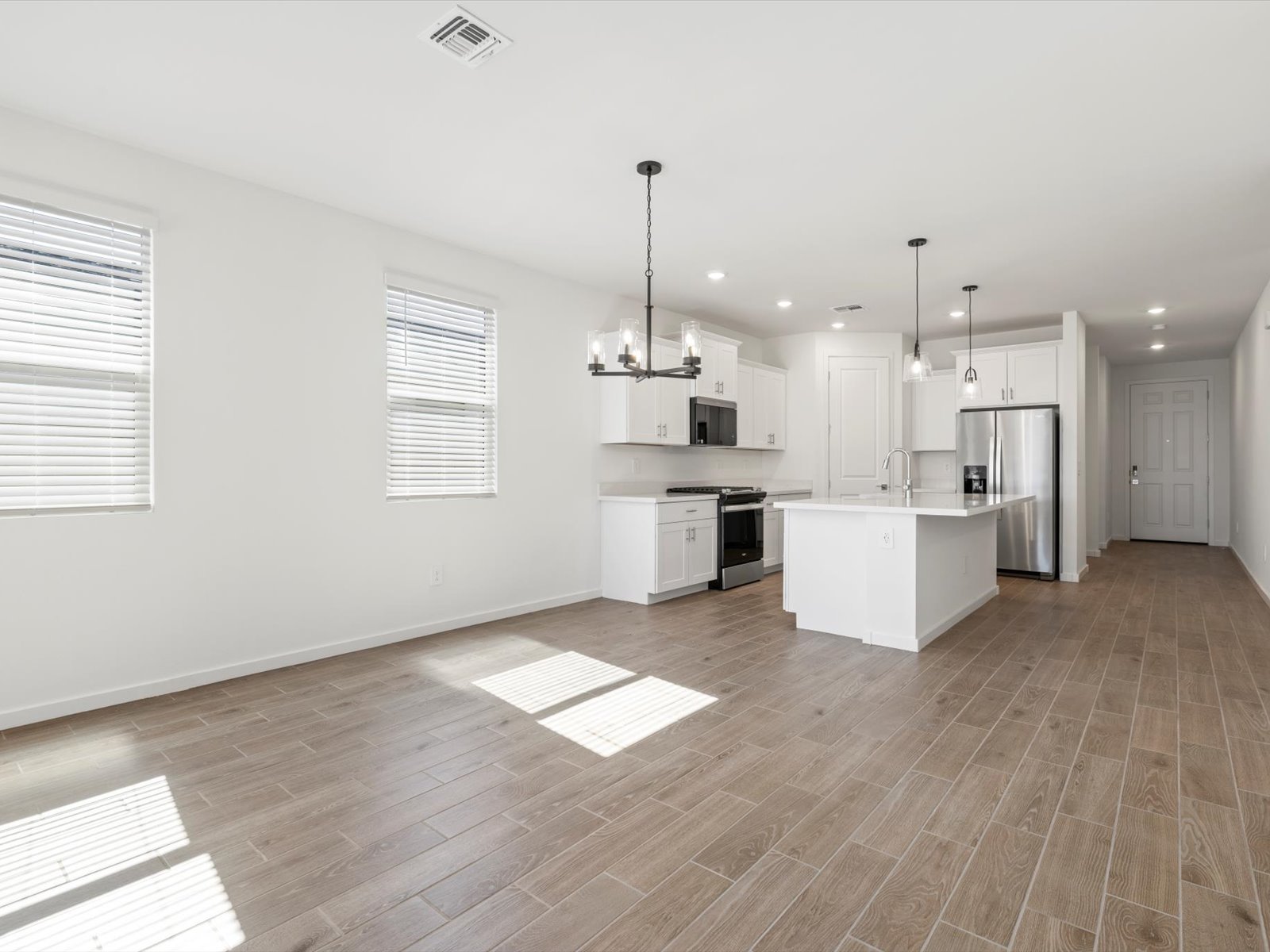 Modern kitchen with white cabinets, stainless steel appliances, island, and wood-look tile flooring in an open, bright space with two windows.