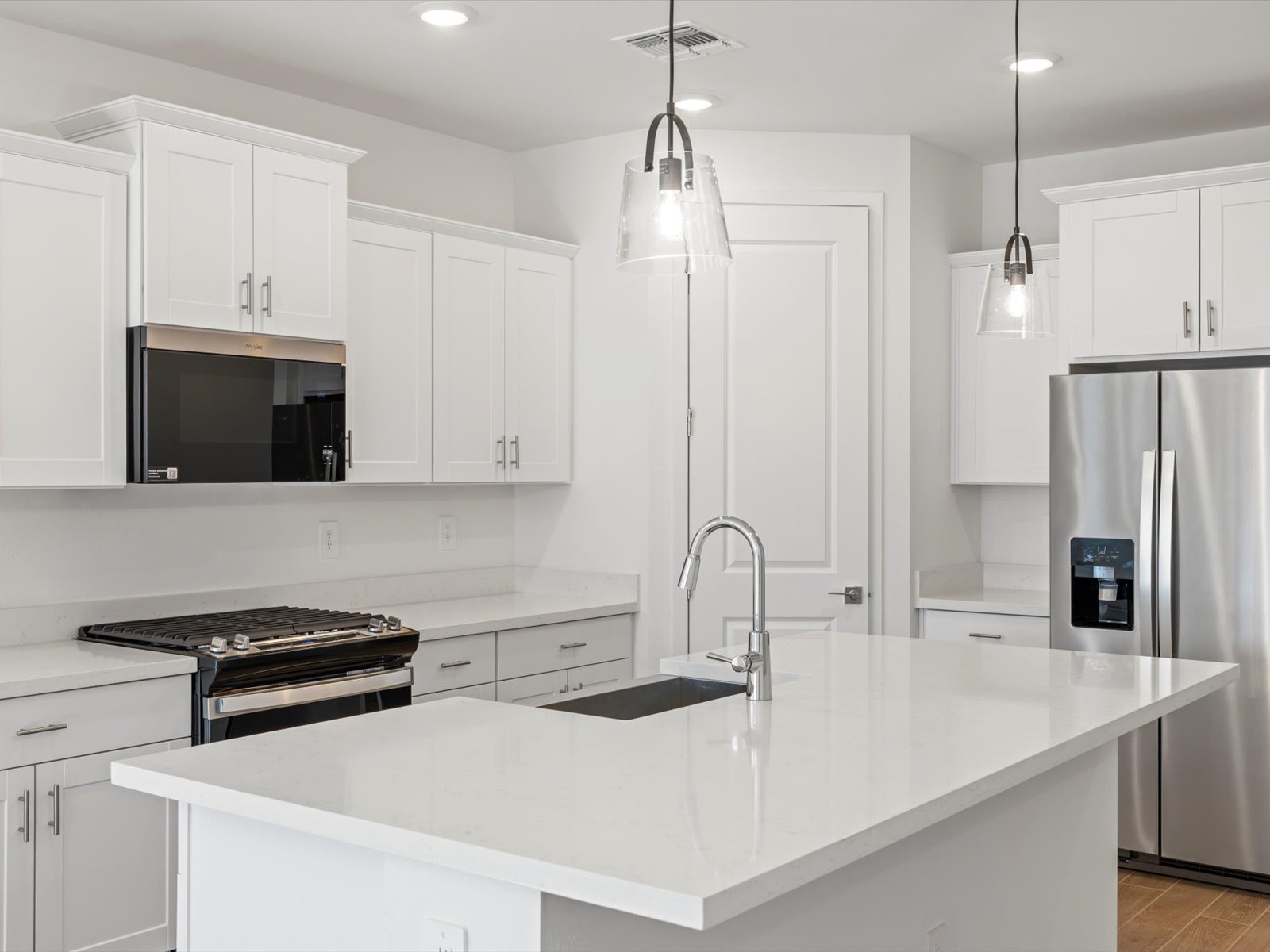 Modern kitchen with white cabinets, stainless steel appliances, an island with a sink, pendant lights, and a gas stove. The space is bright and clean with a minimalist design.