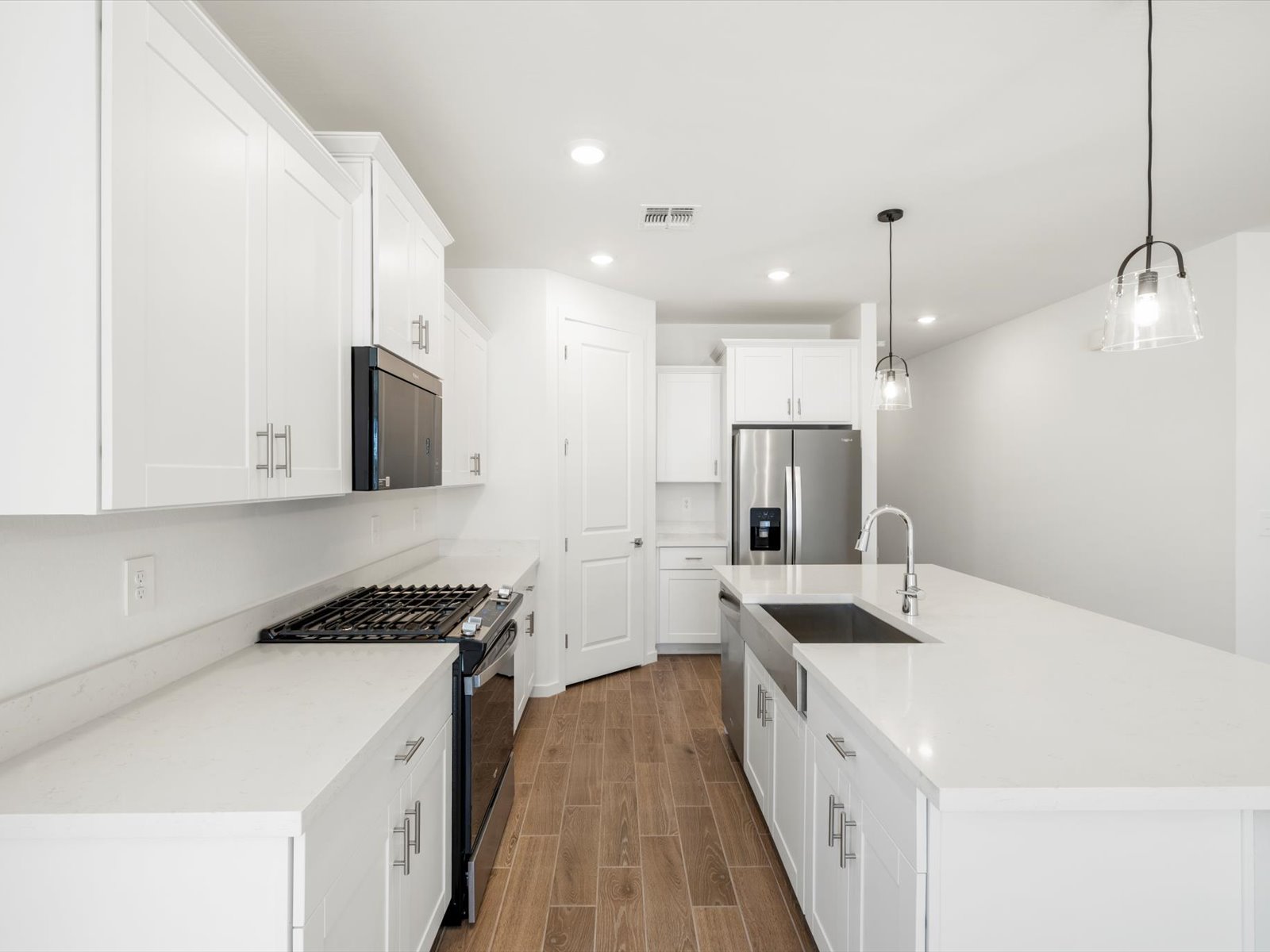 Modern kitchen with white cabinets, stainless steel appliances, gas stove, large island with sink, pendant lights, and wood-look tile flooring.